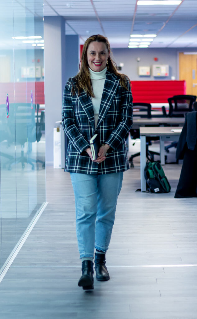Francesca -27 woman in blue dress shirt and blue denim jeans standing beside brown wooden chair